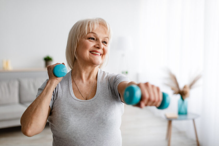 Photo of a smiling older woman performing weight-bearing exercises, showcasing a method of addressing osteoporosis.