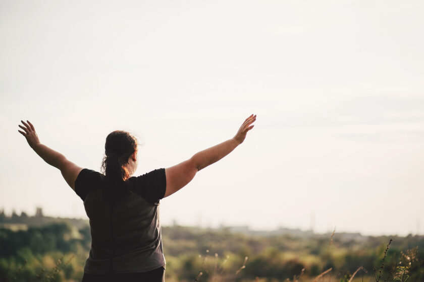 Overweight woman celebrating with raised hands to the sky.