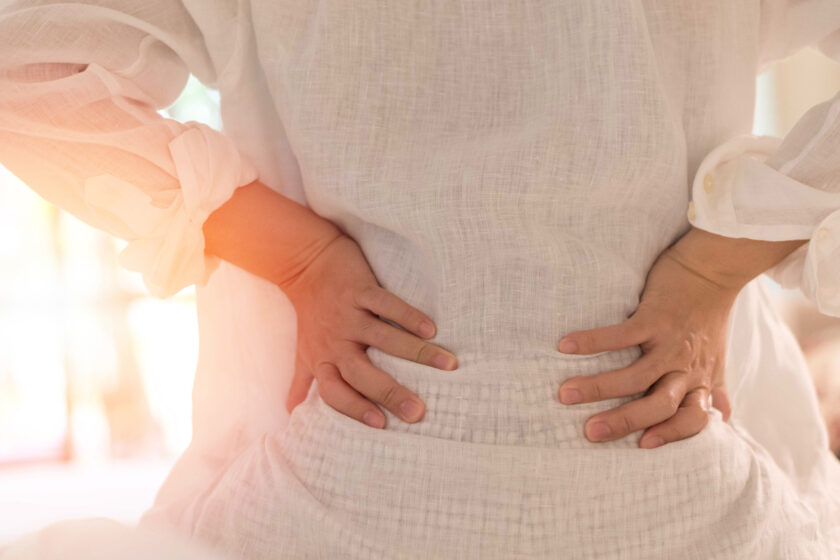 Woman experiencing back pain and holding her back.